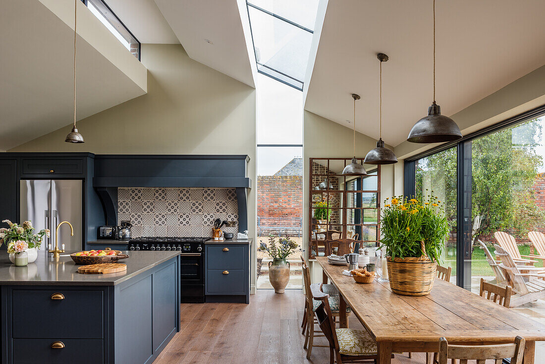 Open-plan kitchen with kitchen island and dining area with rustic dining table and modern skylights