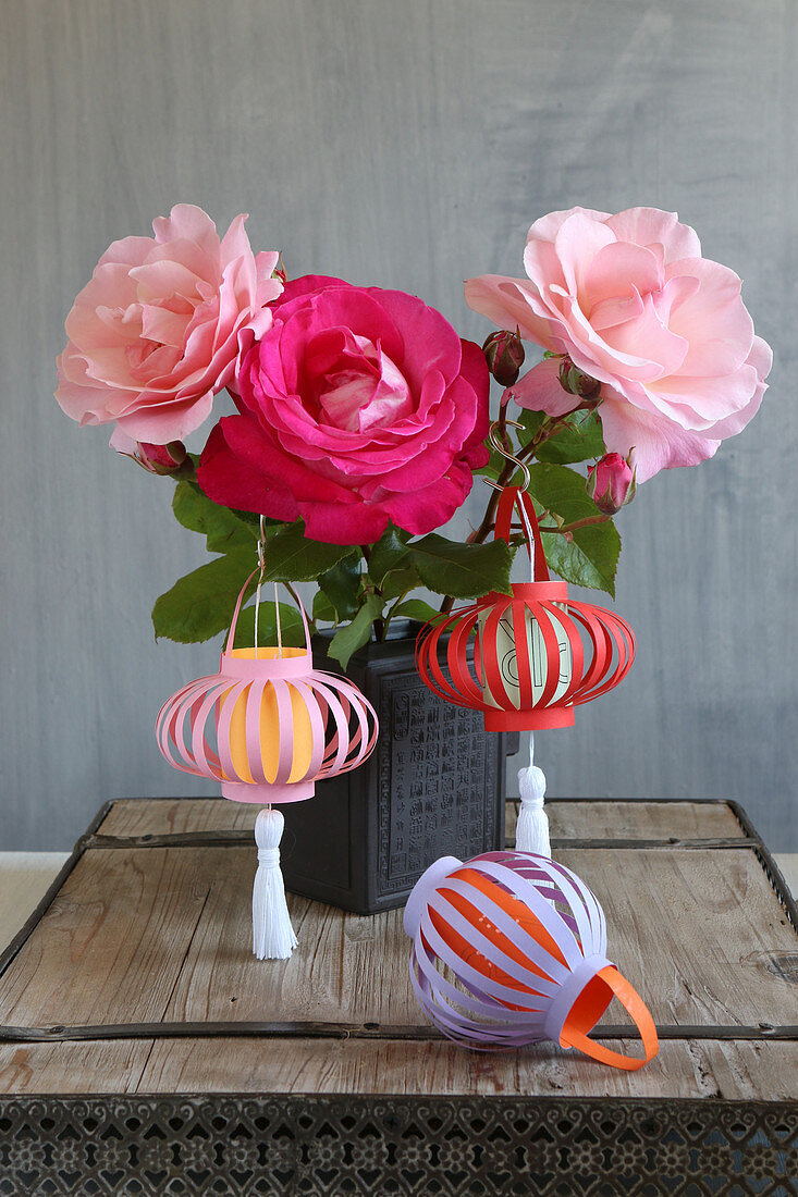 Handmade coloured paper lanterns hung from vase of roses