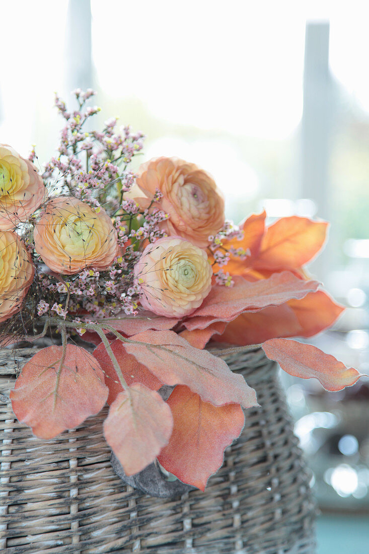 Strauß aus apricotfarbenen Ranunkeln mit Statice auf künstlichem Herbstlaub