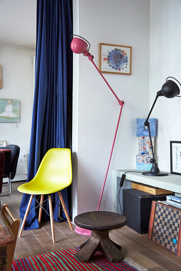 Hocker, gelber Klassikerstuhl, Lowboard und Lampen im Zimmer