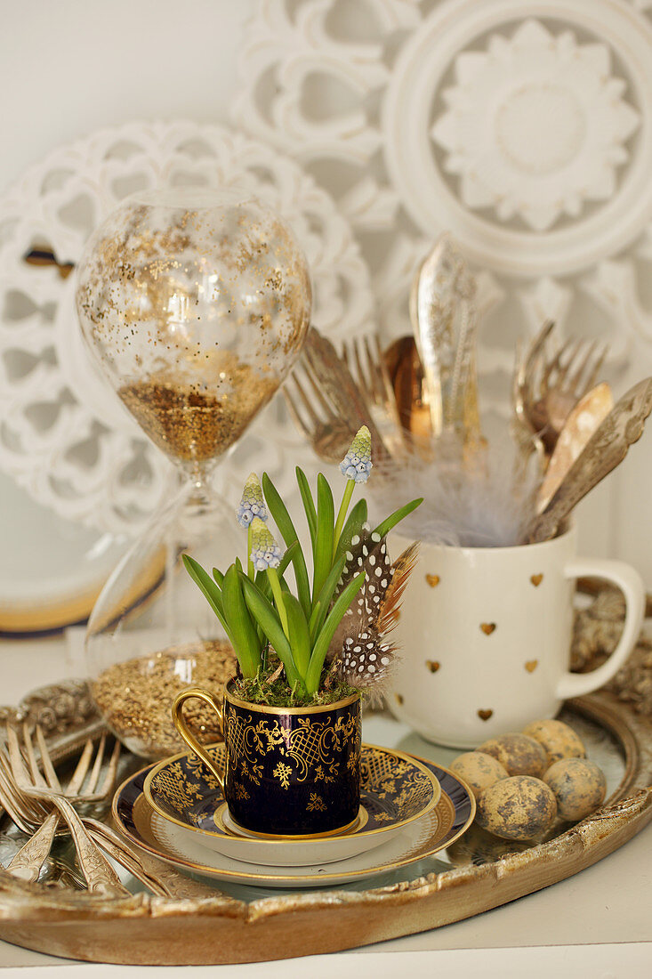 Easter decoration with grape hyacinths in a mug on a tray with silver cutlery, Easter eggs, and an hourglass