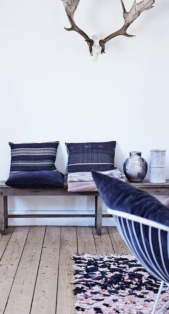 Wooden bench with cushions below antlers on white wall