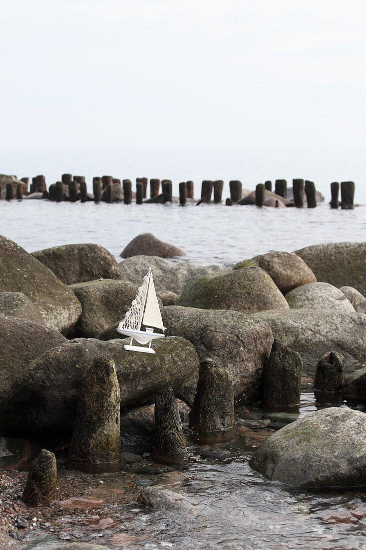 Kleines Modell-Segelboot auf Steinen am Meer