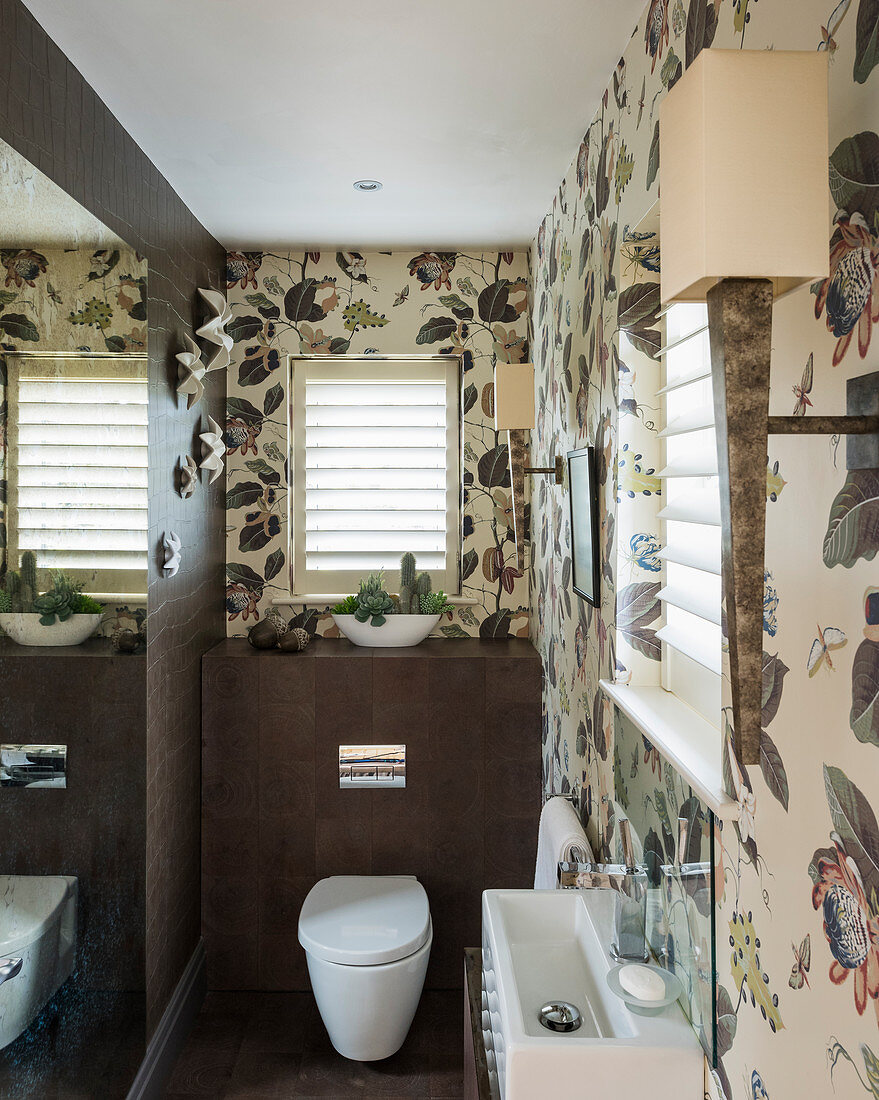 Elegantes Toilettenbad mit floraler Tapete und braunen Fliesen