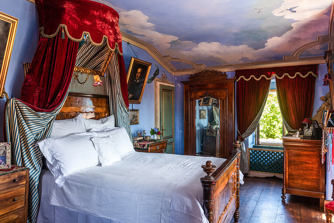 Antique double bed in blue-painted bedroom with ceiling mural