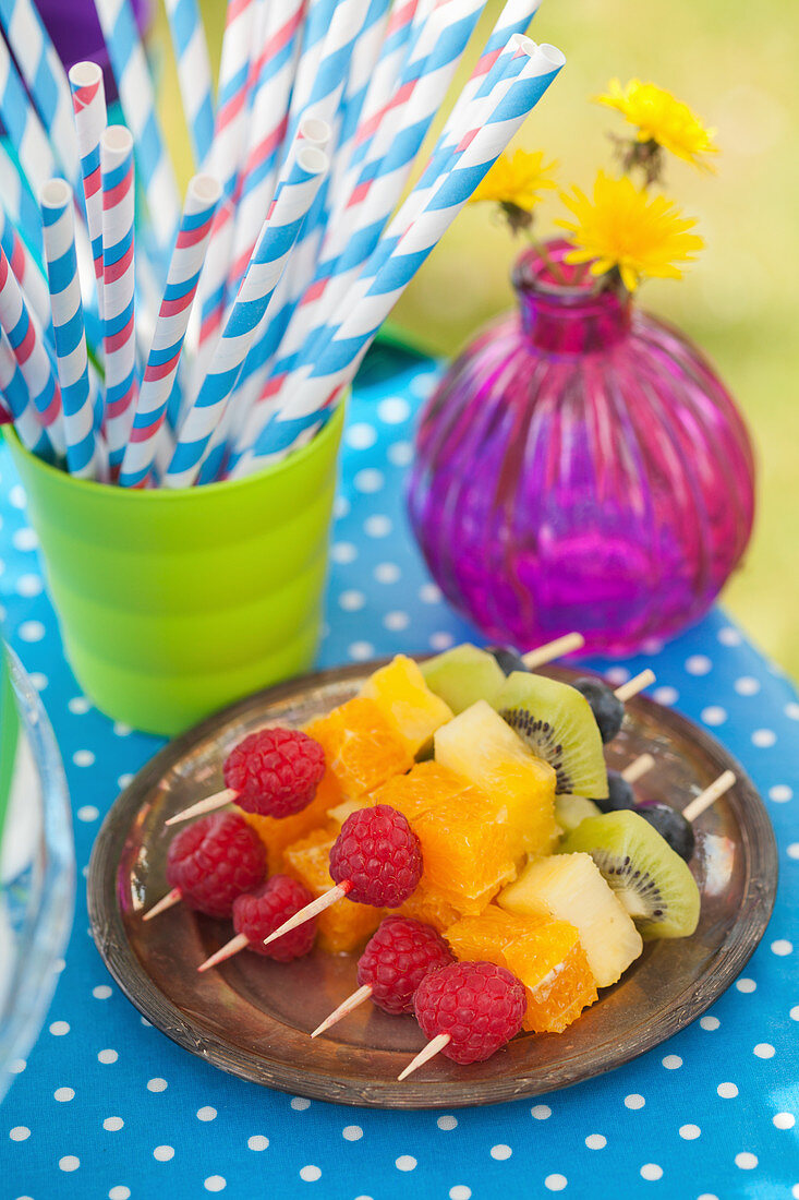 Fruit skewers in rainbow colors and paper straws for a party