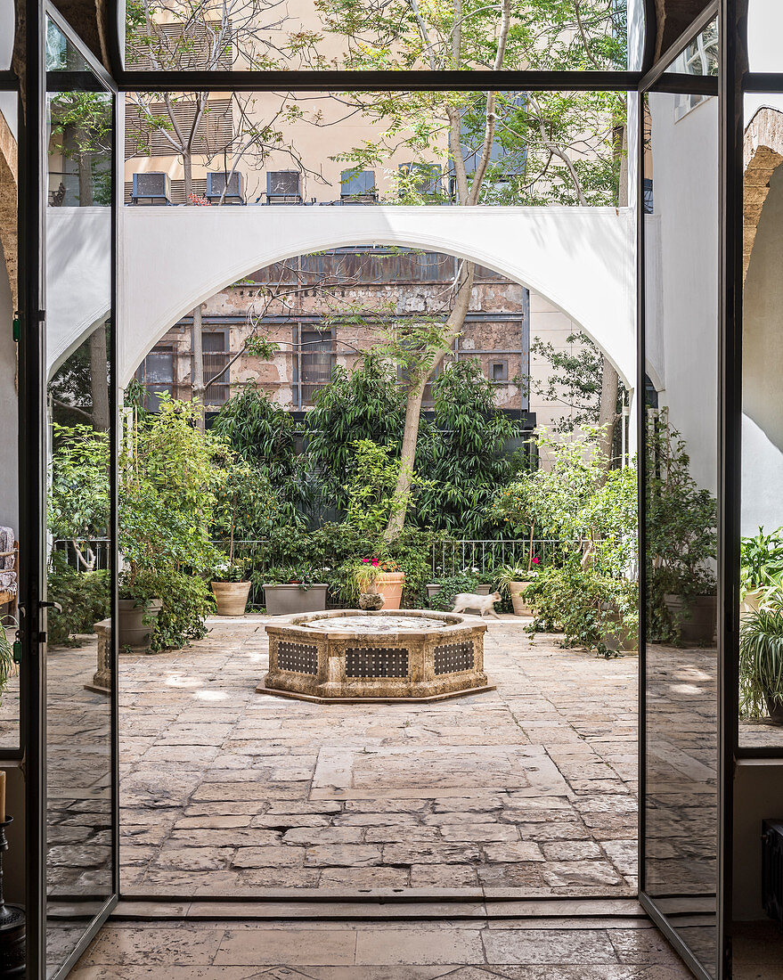 Blick durch moderne Glastür in den Innenhof mit Brunnen und Pflanzen