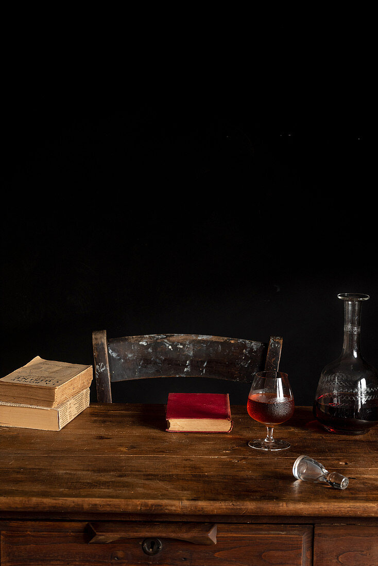 Holztisch mit Glas Cognac, Karaffe und alten Büchern