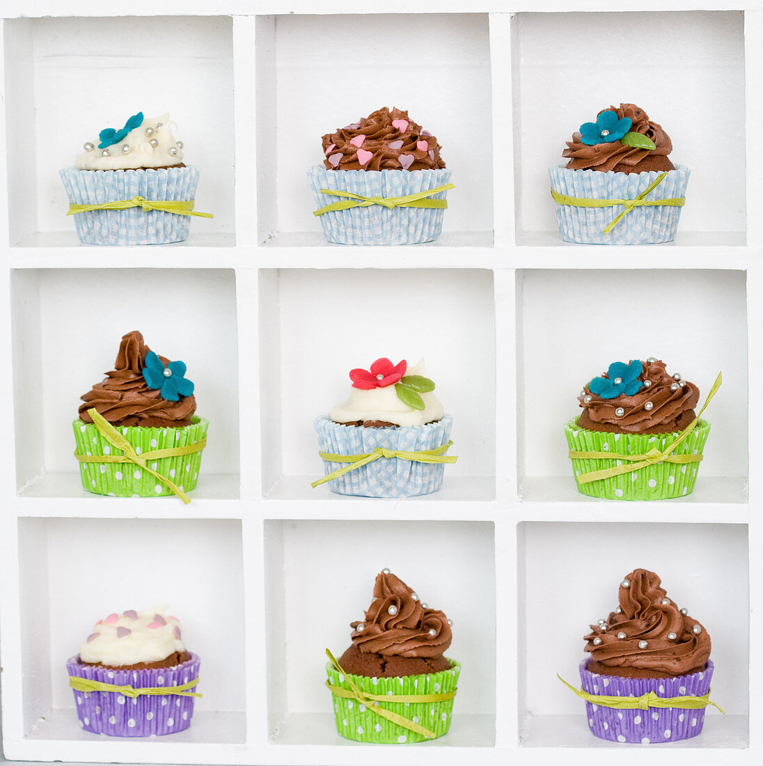Cupcakes mit bunten Manschetten und Zuckerblumen im Setzkasten