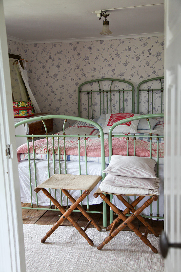 Klapphocker vor grünen Metallbetten im nostalgischen Schlafzimmer