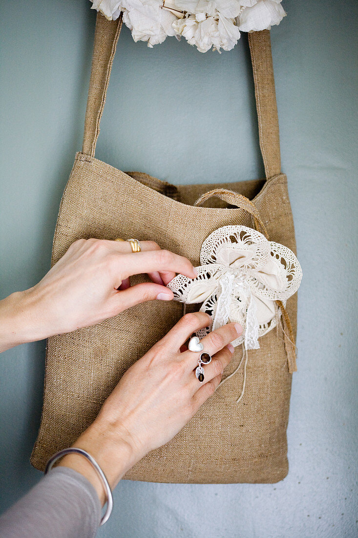 Frauenhände arrangieren Blumenbrosche an einer Stofftasche