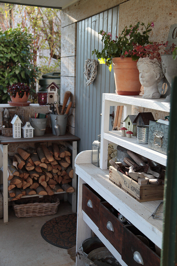 Firewood, gardening utensils and vintage-style decorations on shelves against outside wall
