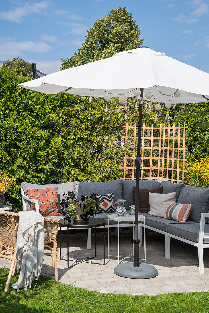 Sonniger Terrassenplatz mit Sitzecke und Sonnenschirm im Garten