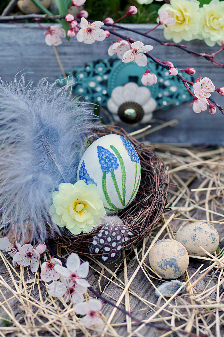 Easter basket with hand-painted Easter egg, feathers, primrose flower, and branch of Cherry plum blossoms