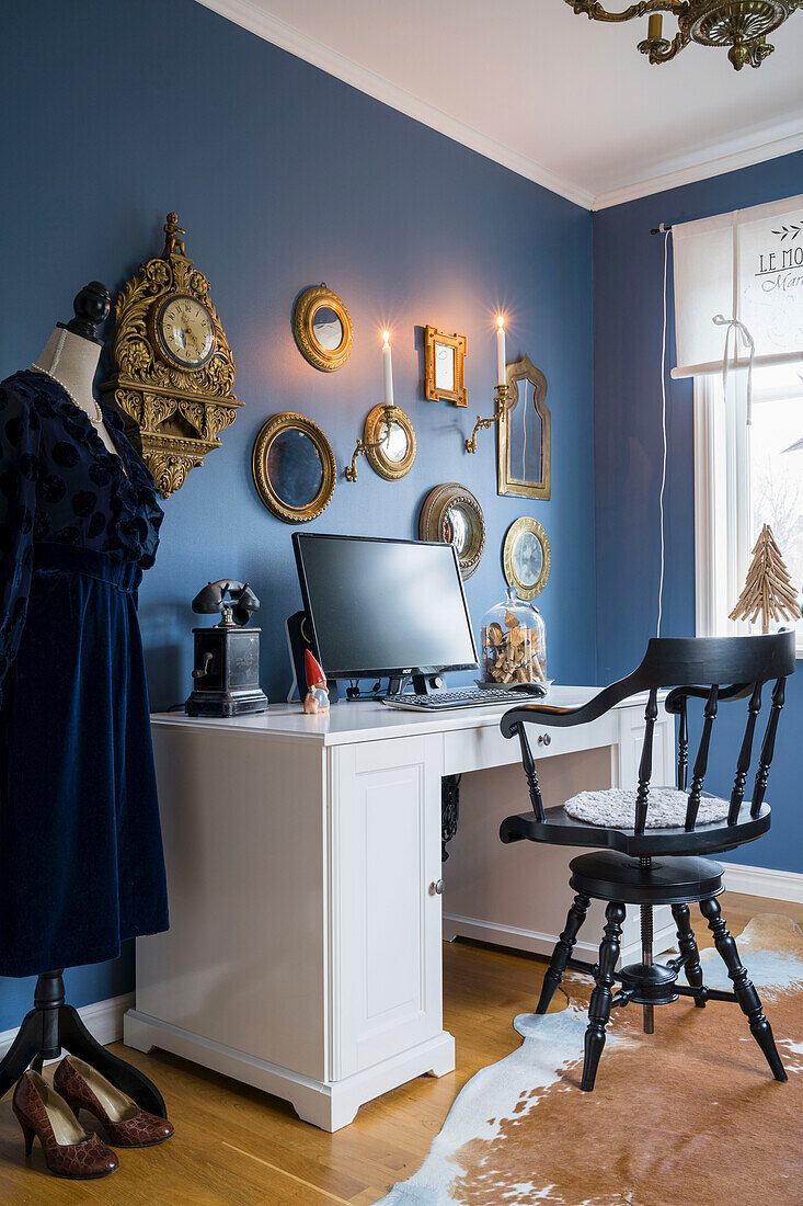 Arbeitszimmer mit blauen Wänden, blaues Kleid auf Schneiderpuppe, antike Uhr und Goldrahmenspiegel and der Wand