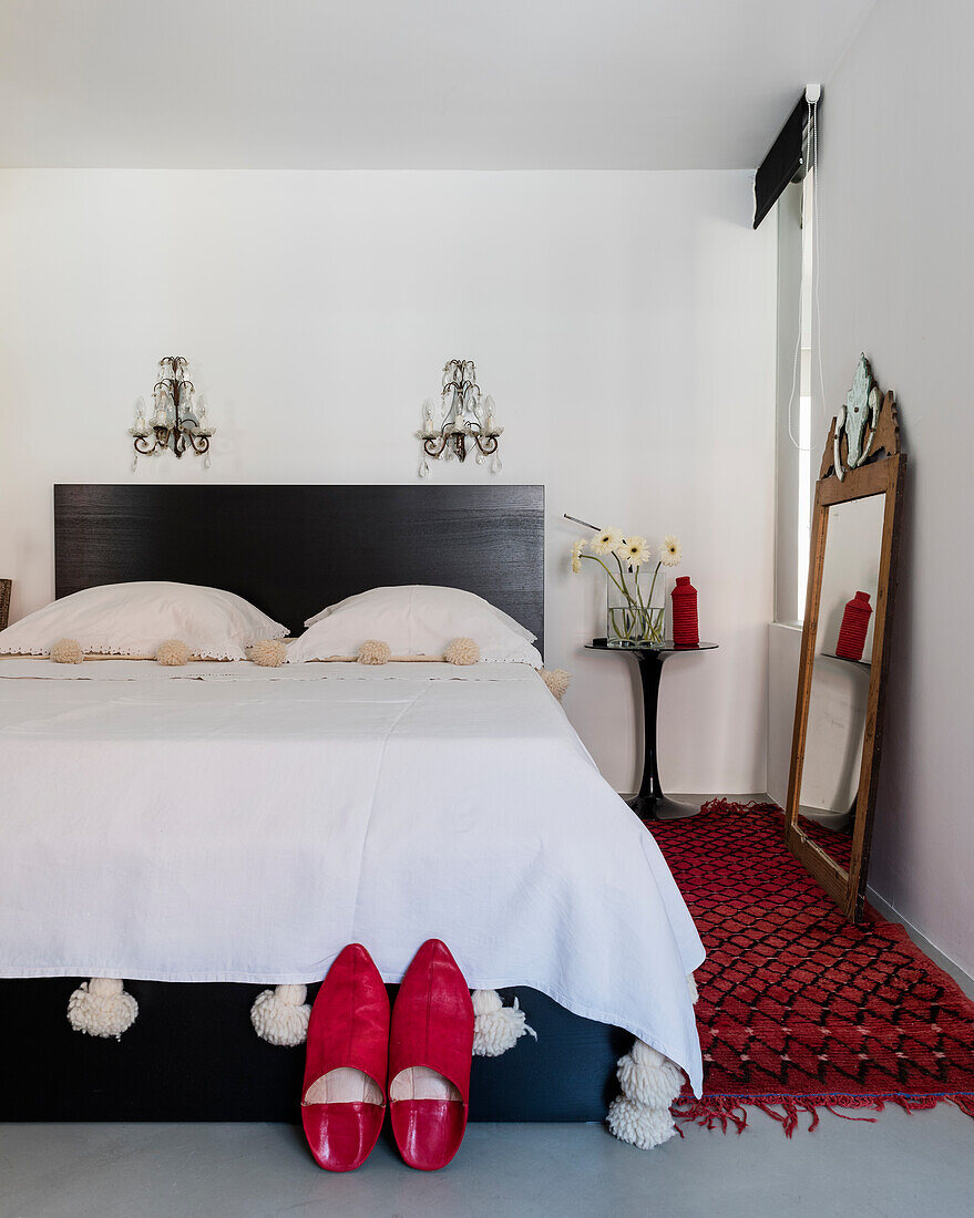 Rote Hausschuhe vorm Bett mit Pompondecke