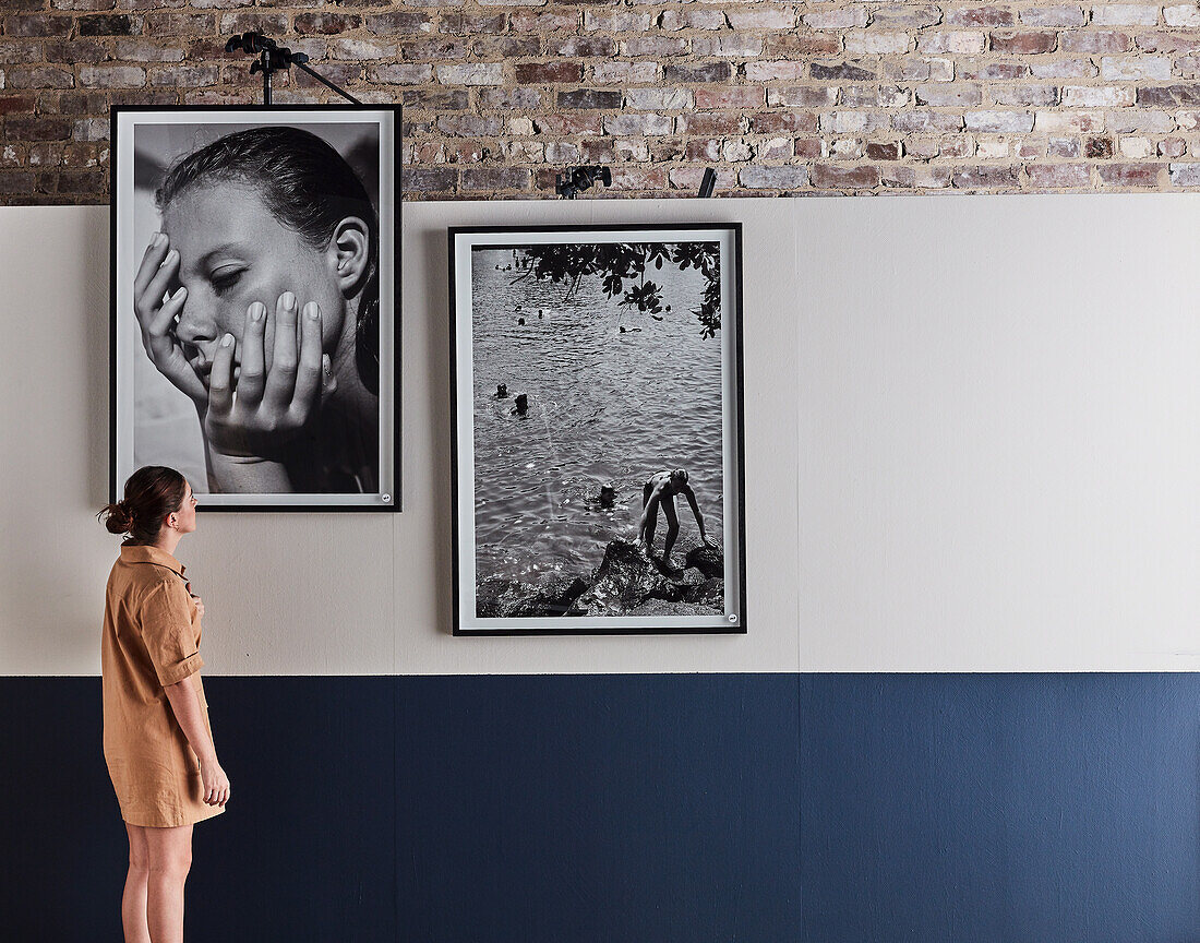 Frau betrachtet großformatige, schwarz-weiße gerahmte Fotos an der Wand