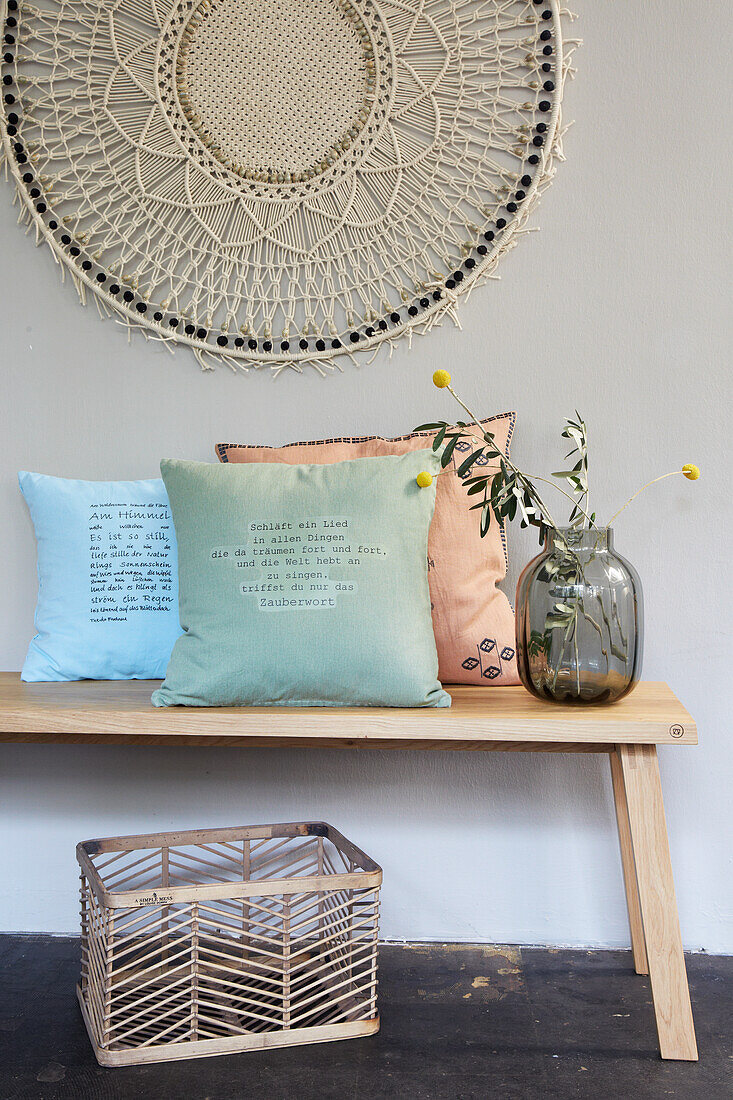 Cushions printed with writing on a wooden bench under macramé wall hanging