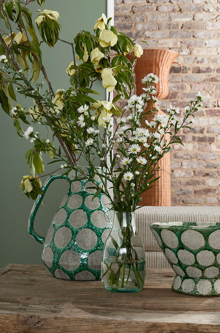 Blumen und Hartriegelzweige in grünem Krug und einer Glasvase