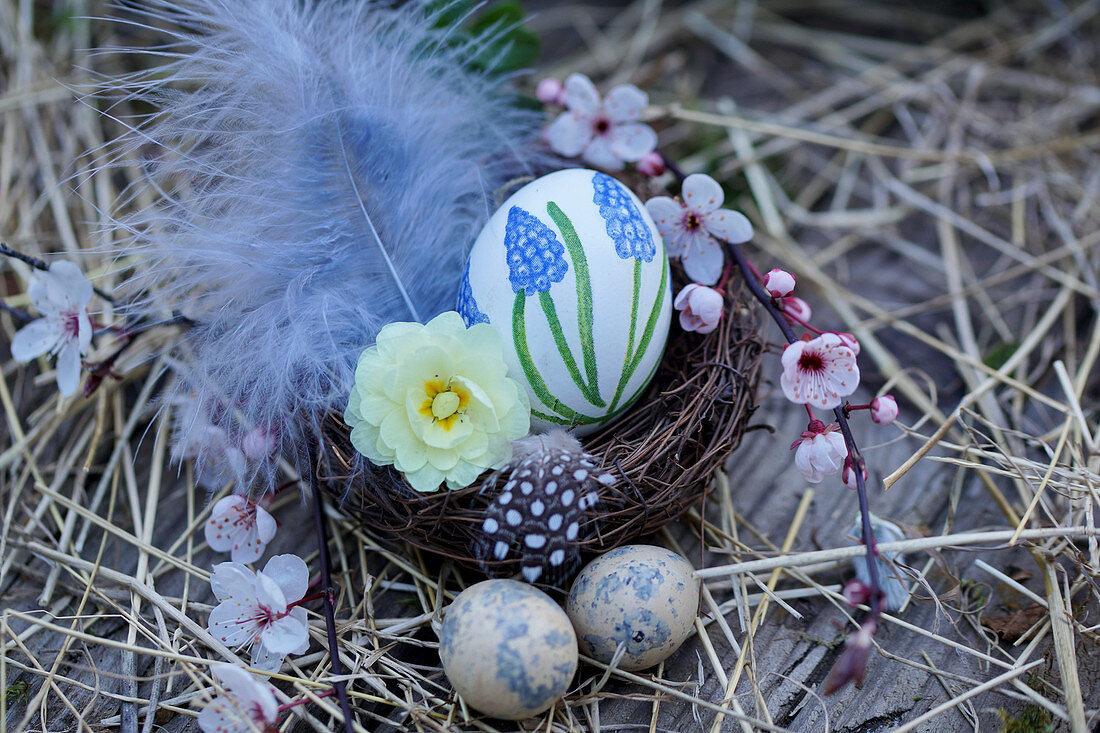 Easter basket with hand-painted Easter egg, filled with primrose flowers and feathers, branches of Cherry plum blossoms, and Easter eggs