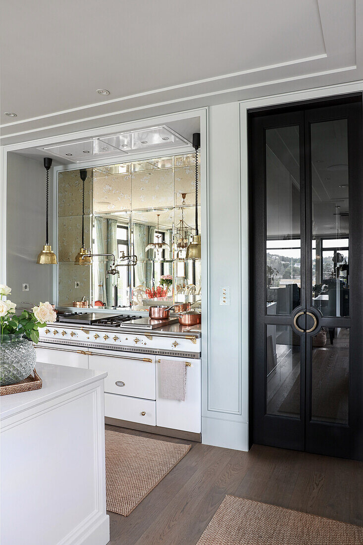 Glastür mit schwarzem Rahmen neben eleganter Küchenzeile mit Spiegelwand