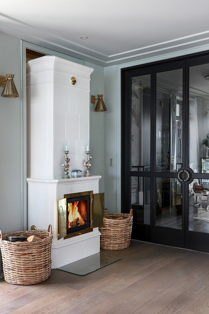 White, Swedish tiled stove next to glass doors with black frame