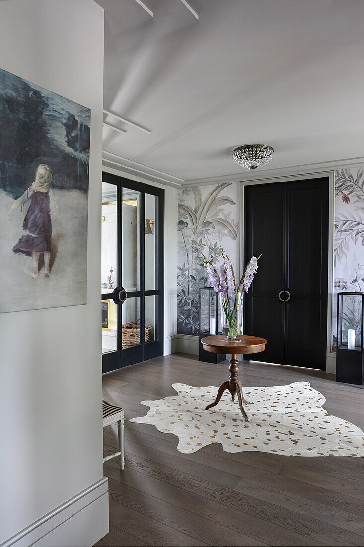 Antiker, runder Tisch mit Gladiolen auf Tierfellteppich in elegantem Vorraum mit Tapete