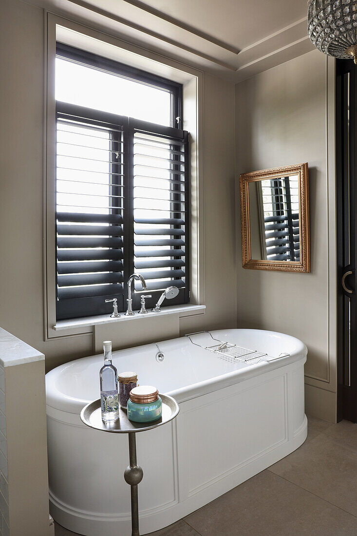 White, free-standing bathtub below window with louvre blinds in bathroom