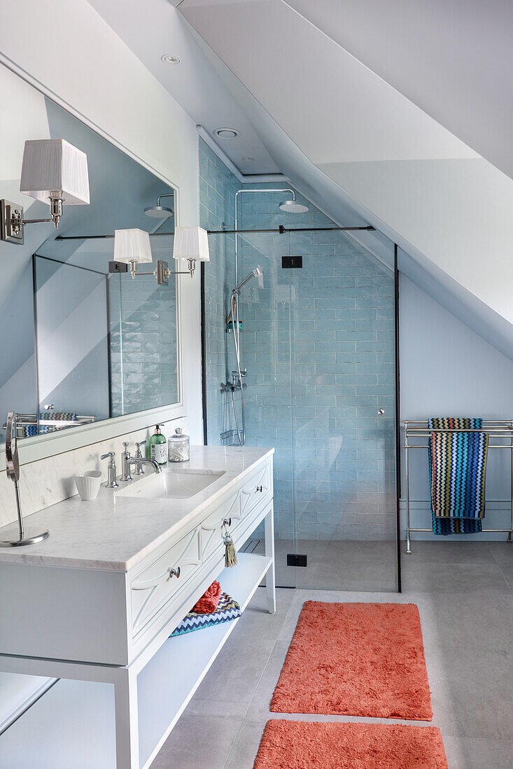 Salmon-pink bath rugs, white washstand and shower area with glass screen
