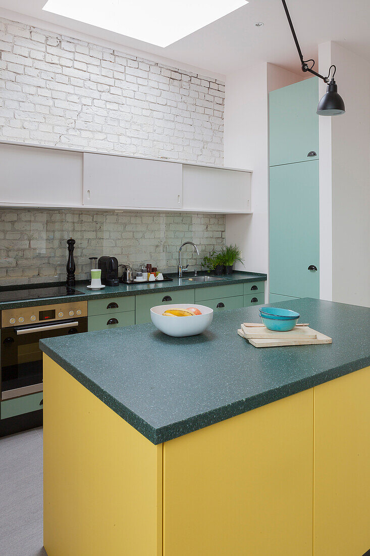 Kücheninsel mit gelber Front in offener Küche mit weiß gestrichener Ziegelwand
