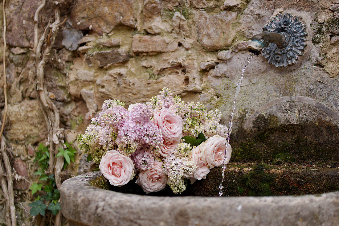 Fragrant spring bouquet of lilacs and roses in basin of wall fountain