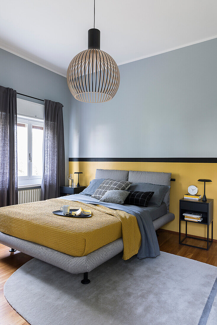 Doppelbett mit grauem Bettkopfteil und gelber Tagesdecke