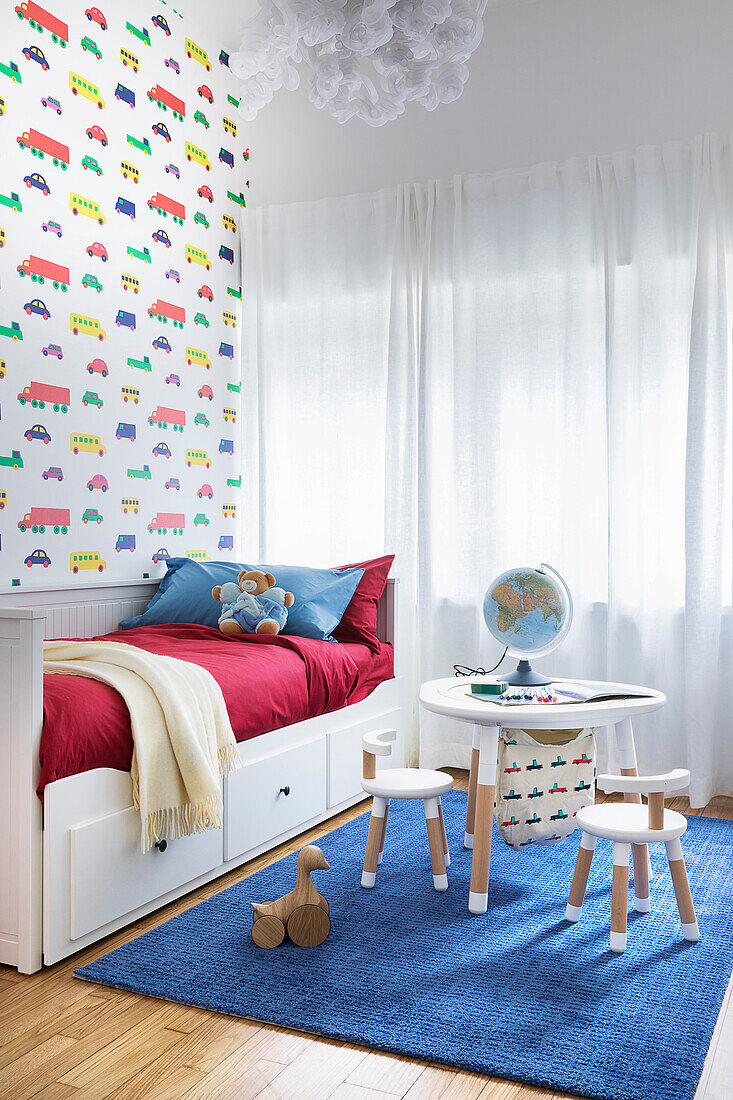 White bed, children's table and chairs and wallpaper with a car motif in boys' bedroom