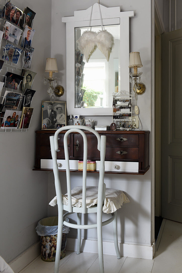 Chair at wall-mounted dressing table and family photos in postcard rack