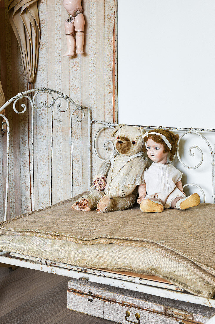 Teddy und Puppe auf einem alten Metallbett mit Jutematratze