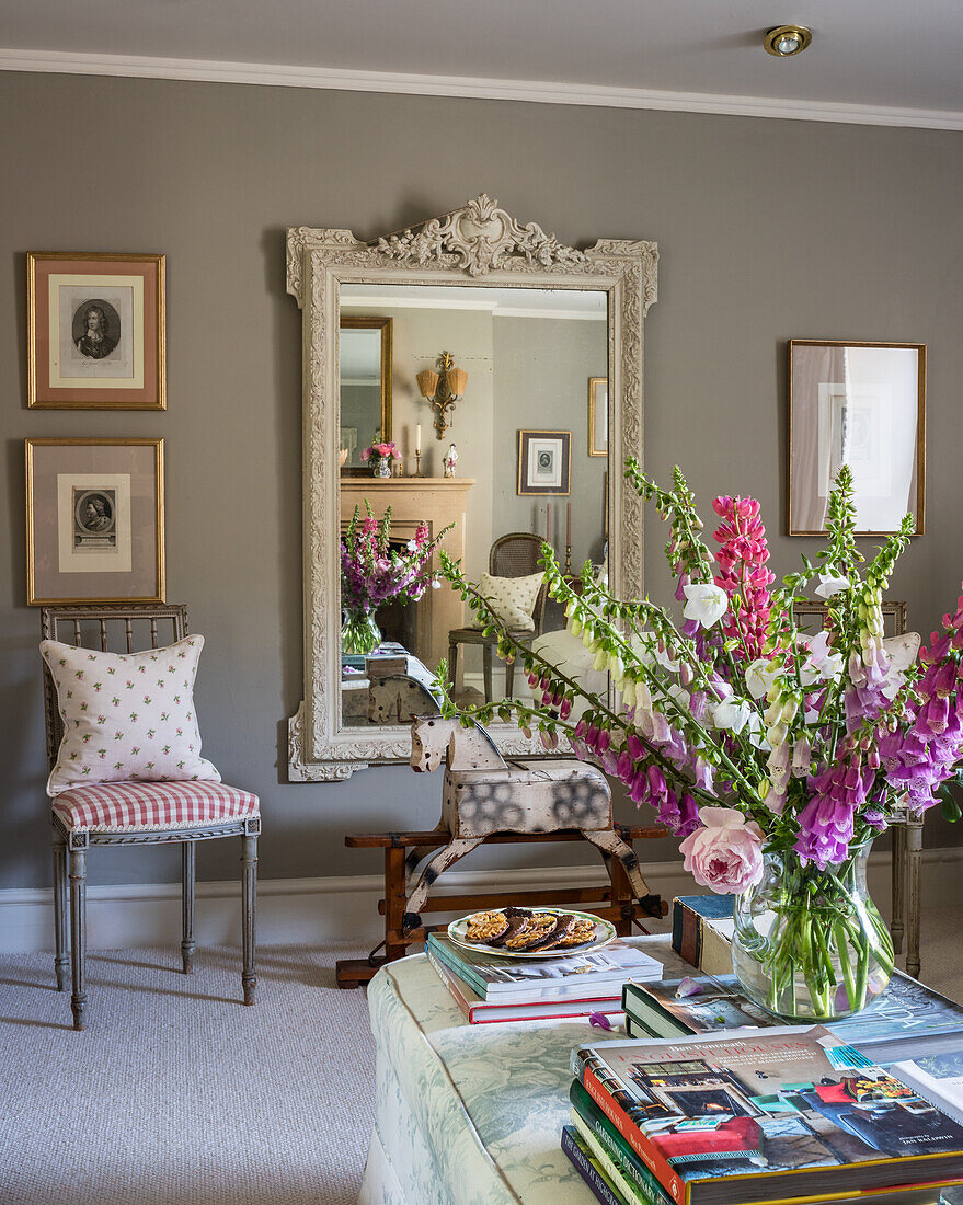 Antikes Schaukelpferd und dekorativer französischer Spiegel, im Vordergrund Couchtisch mit Gartenblumen