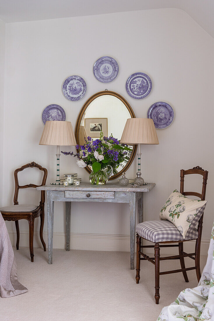 Antique, decorative wall plates and oval mirror above old wooden table