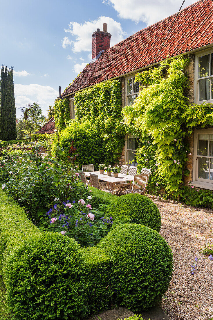 Englisches Landhaus mit Garten und begrünter Fassade, Tisch mit Stühlen auf der Terrasse