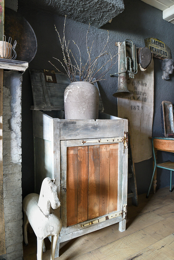 Vase mit Zweigen in einer Schütte vor grauer Wand mit Vintage-Deko