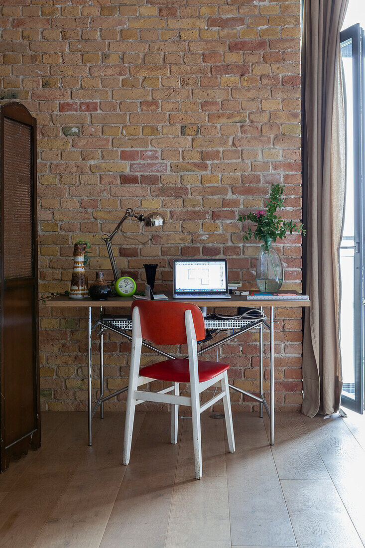 Schreibtisch mit rotem Stuhl vor Ziegelwand