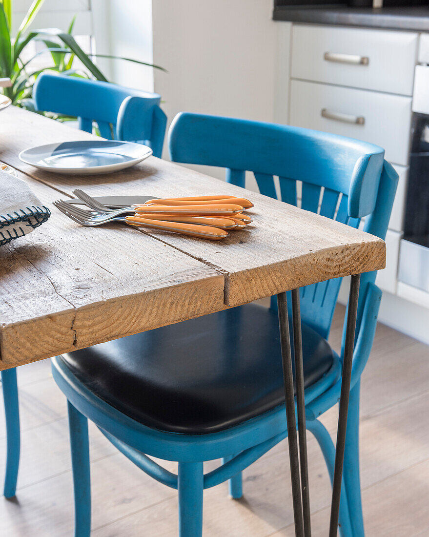 Esstisch aus Holzbrettern und blaue Stühle, Gabeln auf Tischplatte