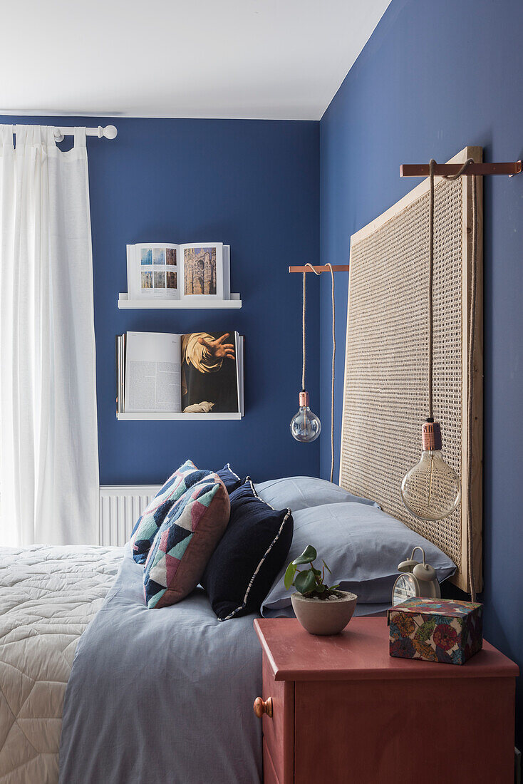 Doppelbett im Schalfzimmer mit blauen Wänden, hängende Glühbirne über dem Nachttisch
