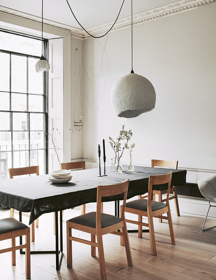 Dining table with grey tablecloth, chairs and pendant lamps in front of window