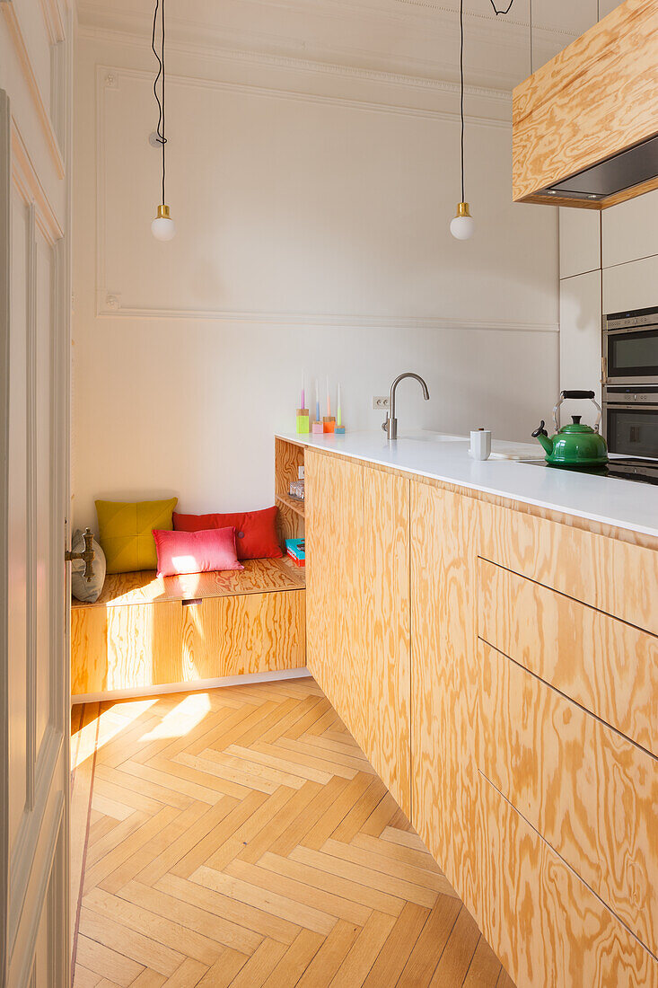 Kitchen counter with light plywood front and integrated bench with colourful scatter cushions
