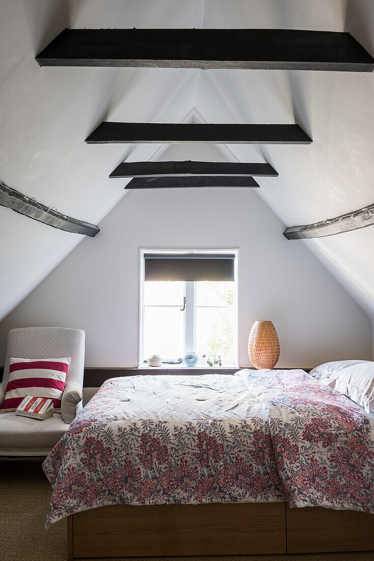 Doppelbett mit geblümter Tagesdecke in einfach eingerichtetem Schlafzimmer im Dachgeschoss