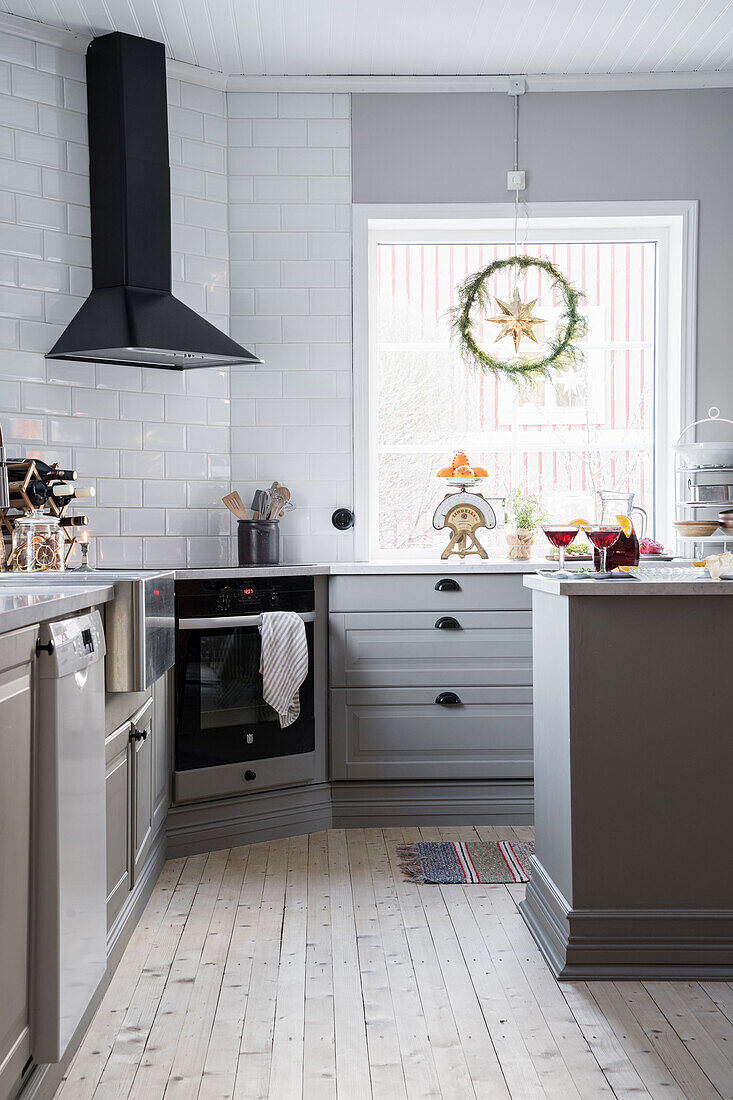 Graue Unterschränke und Dunstabzugshaube in Küche mit weißen Wandfliesen und Holzdielenboden