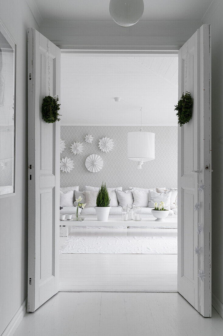Blick durch geöffnete Flügeltüren in helles Wohnzimmer mit DIY-Couchtisch, Polstersofa und weiße Papiersterne