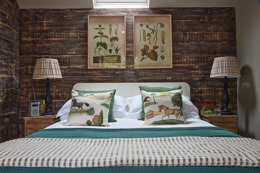 Doppelbett, darüber botanische Zeichnungen im Schlafzimmer mit rustikaler Bretterwand