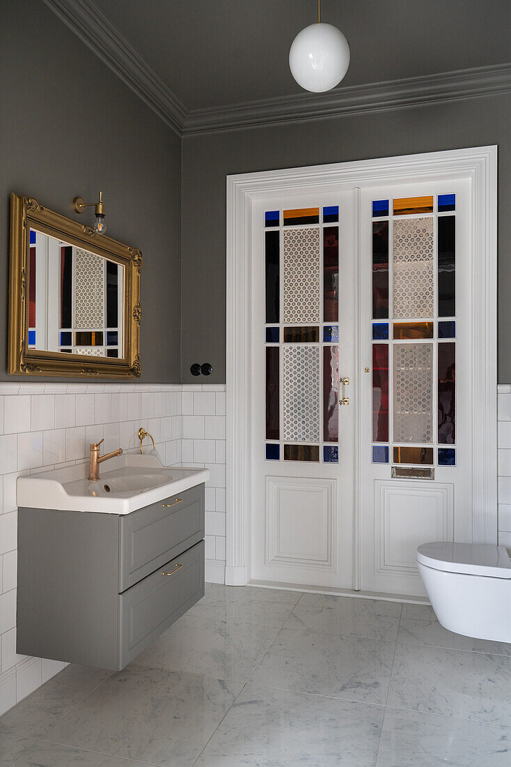 Double doors with wainscoting and stained glass in a classic bathroom in grey and white
