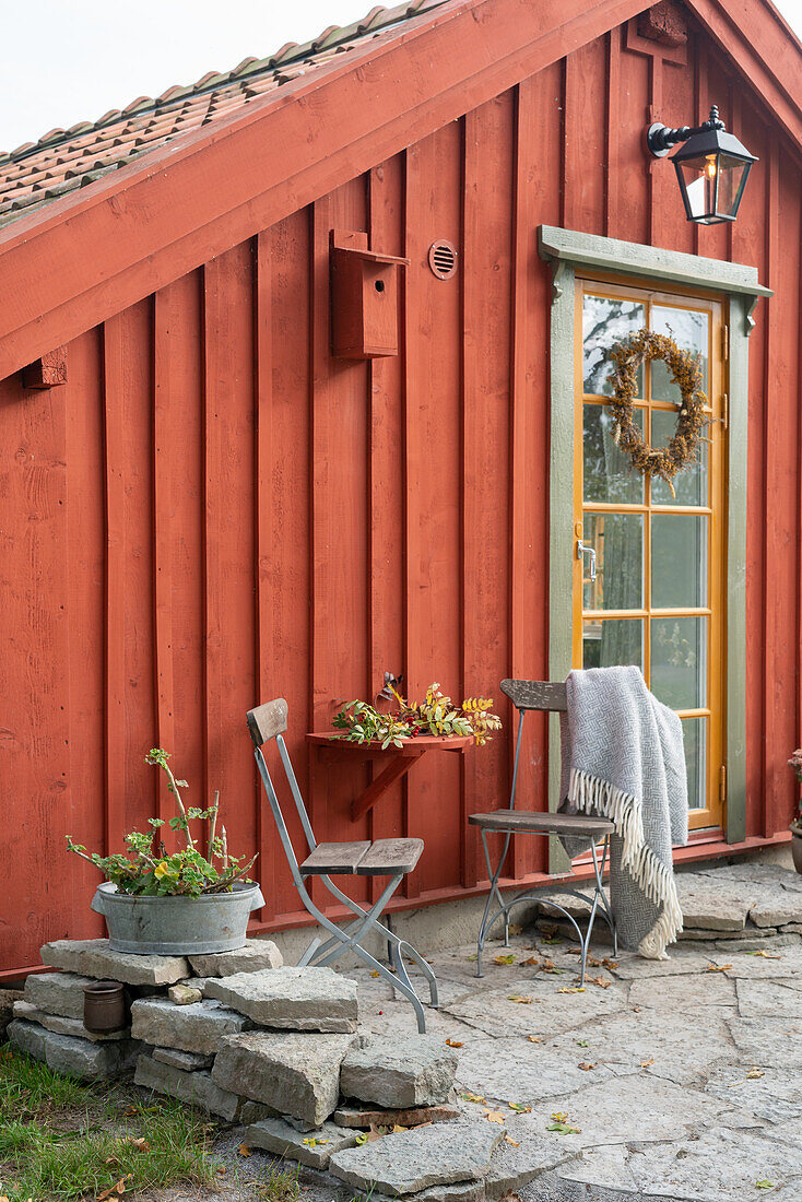 Kleiner Sitzplatz vor rot-braunem Holzhaus mit Sprossentür